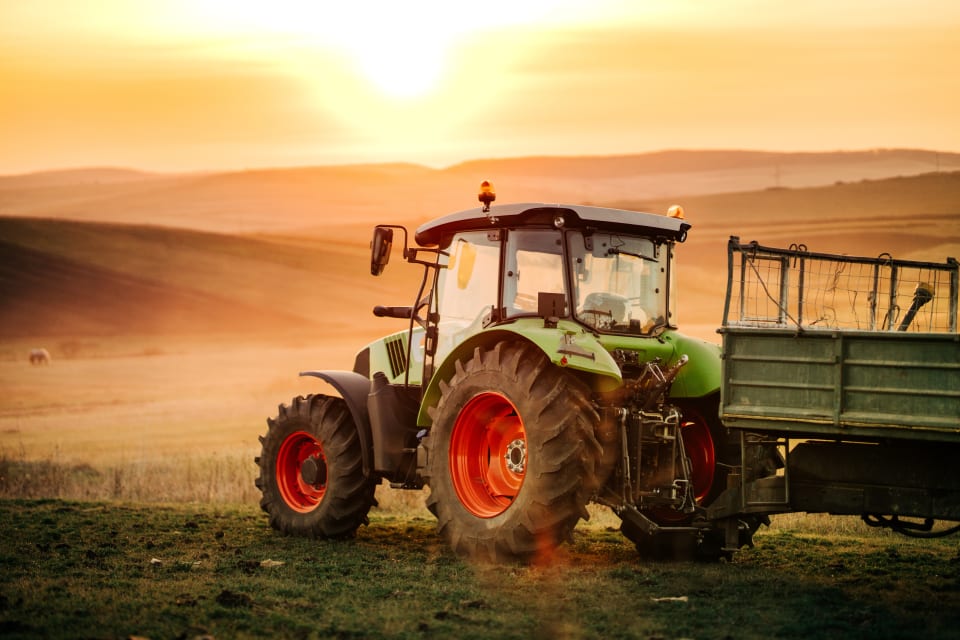 A tractor with telematics at work in a field, there's a beautiful sunset in the background