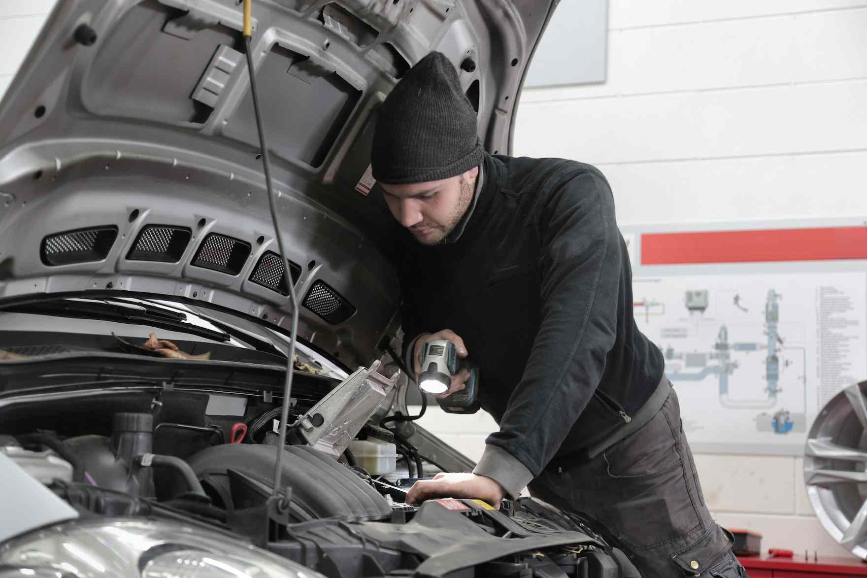 A man in a black beanie hat looks under the bonnet of a car made by the volkswagen car manufacturers that has the volkswagen polo model name