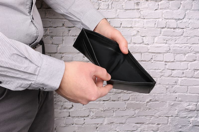 A male, small business owner holds an empty wallet because he used all his cash to cover an important business expense