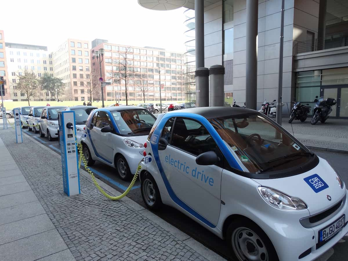 Six white electric cars being charged at a public charging station