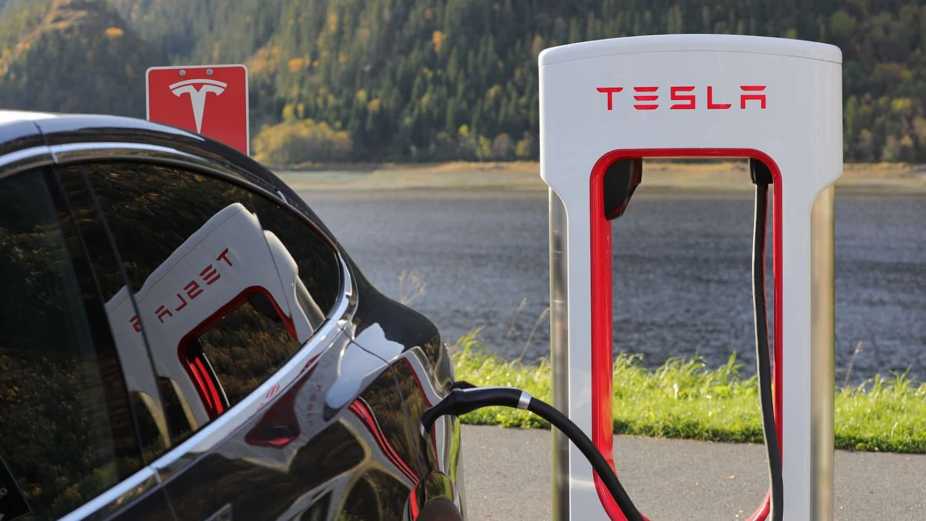 A black Tesla is charged at a Tesla charging point by a lake