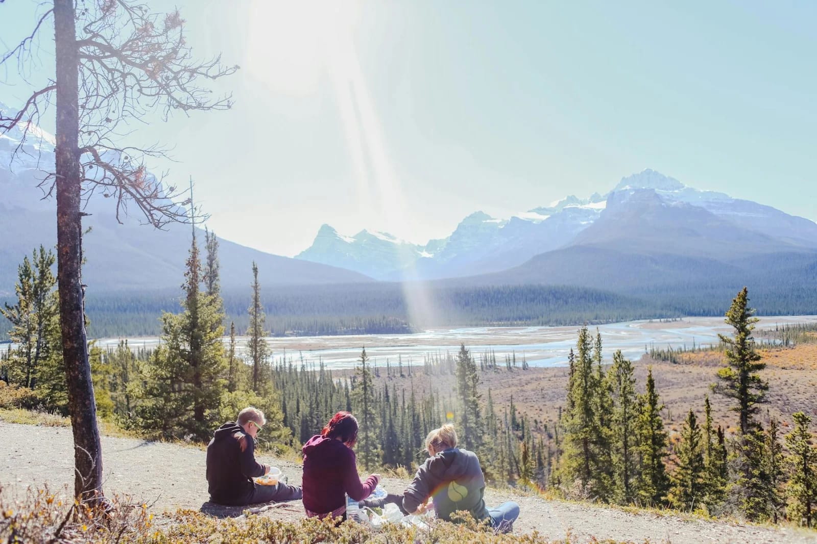 Grupo de personas sentadas en el suelo durante una salida al aire libre entre árboles y montañas