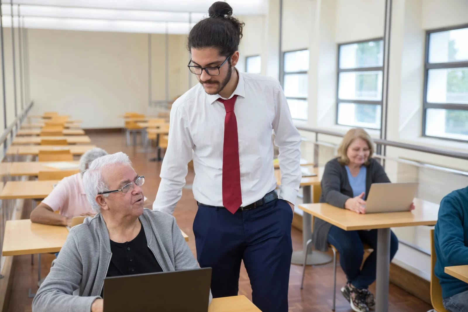 Un monitor enseña a un grupo de personas mayores a usar ordenadores en un aula de informática