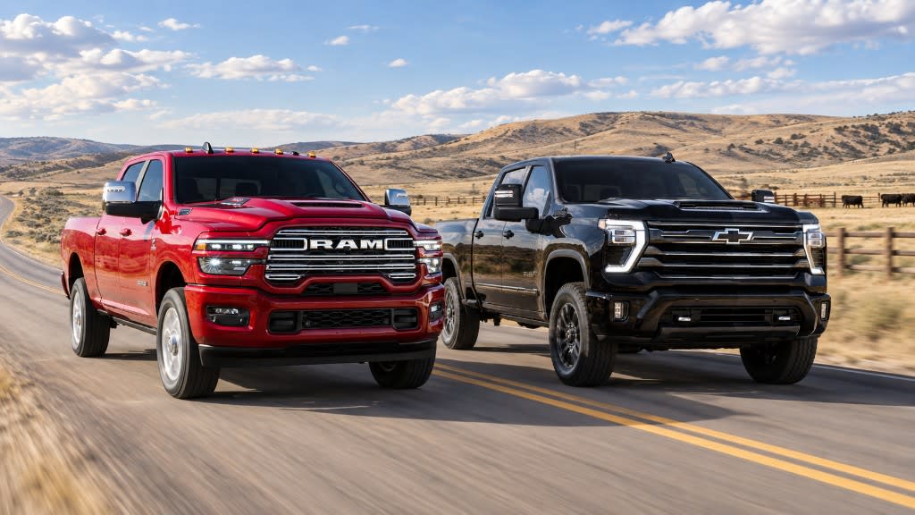 Red 2026 Ram 2500 and black 2026 Chevrolet Silverado 2500 HD driving side by side on a rural road