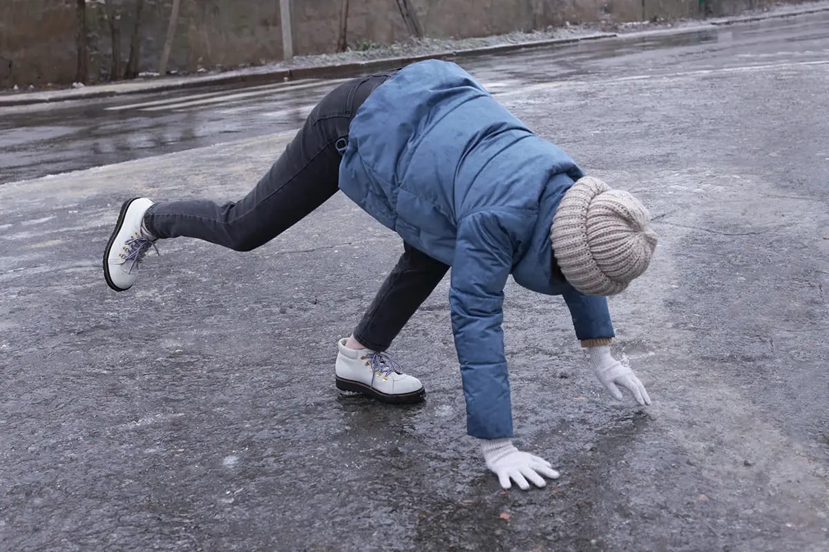 Young woman having difficulty walking on an icy surface in winter