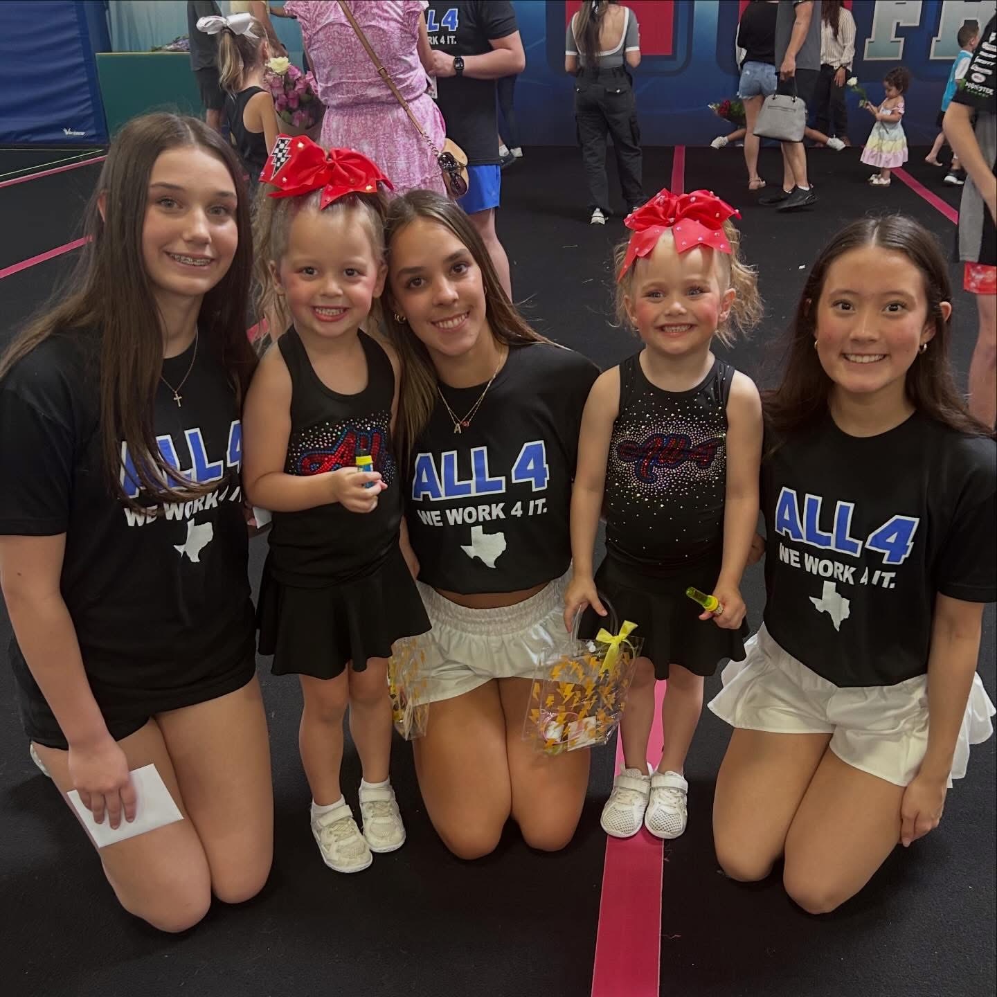Two young cheerleaders with red bows posing with three older All 4 athletes