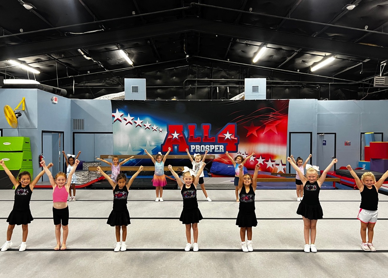 Tier 1 cheer class lined up with arms raised in a V on the All 4 Prosper floor