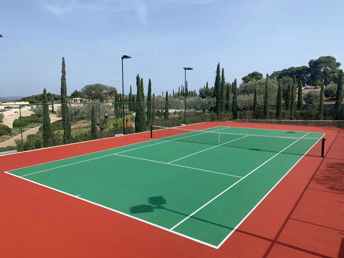 Floodlit hard tennis court framed by cypress and olive trees at Amanzoe, Greece