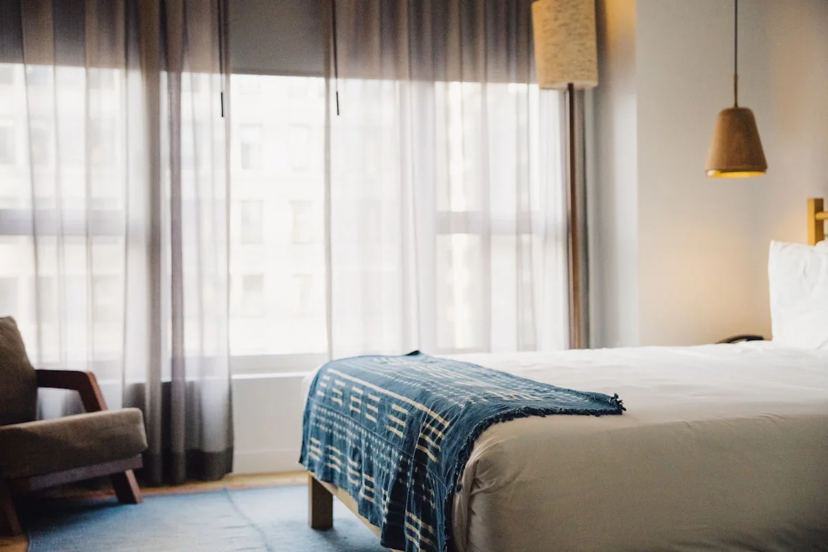 Modern hotel room with sheer curtains and a city view, the kind of base room a suite upgrade improves on