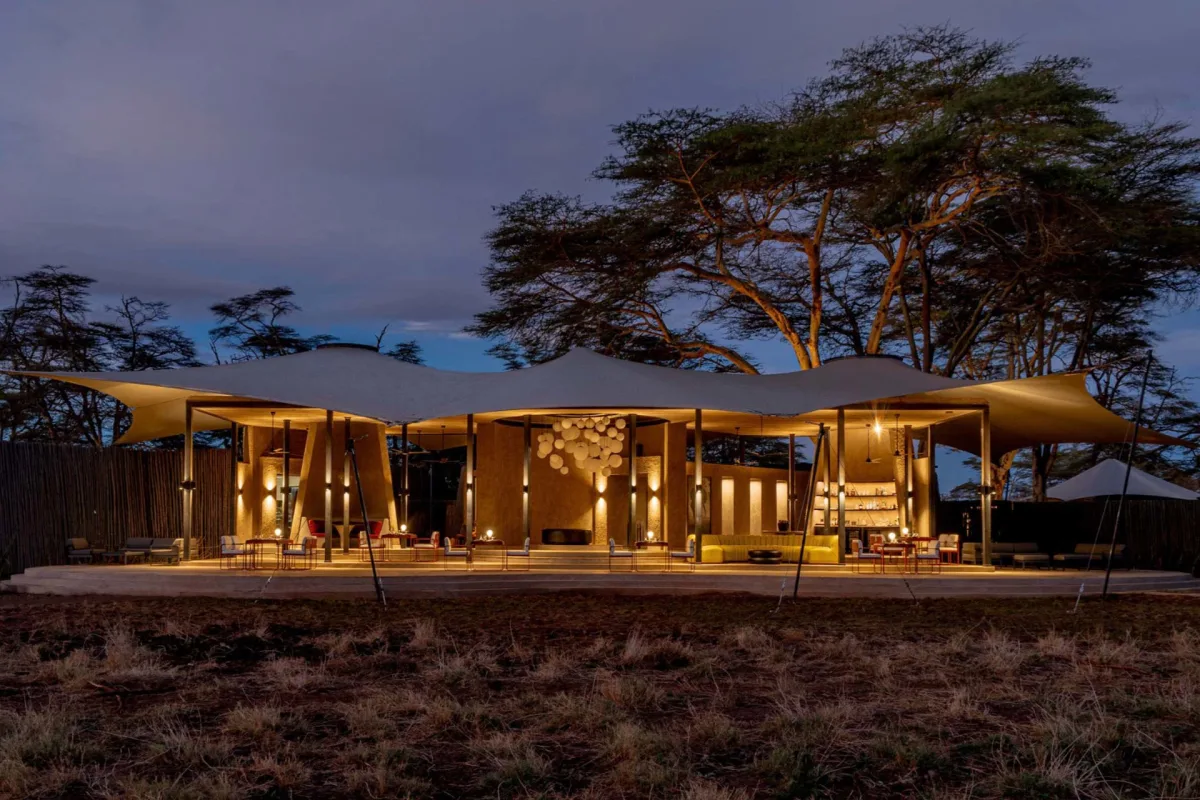 The tented main guest area at Angama Amboseli lit at dusk beneath acacia trees