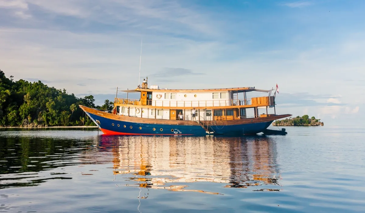 Rascal phinisi yacht at anchor off a jungle-covered island in Indonesia