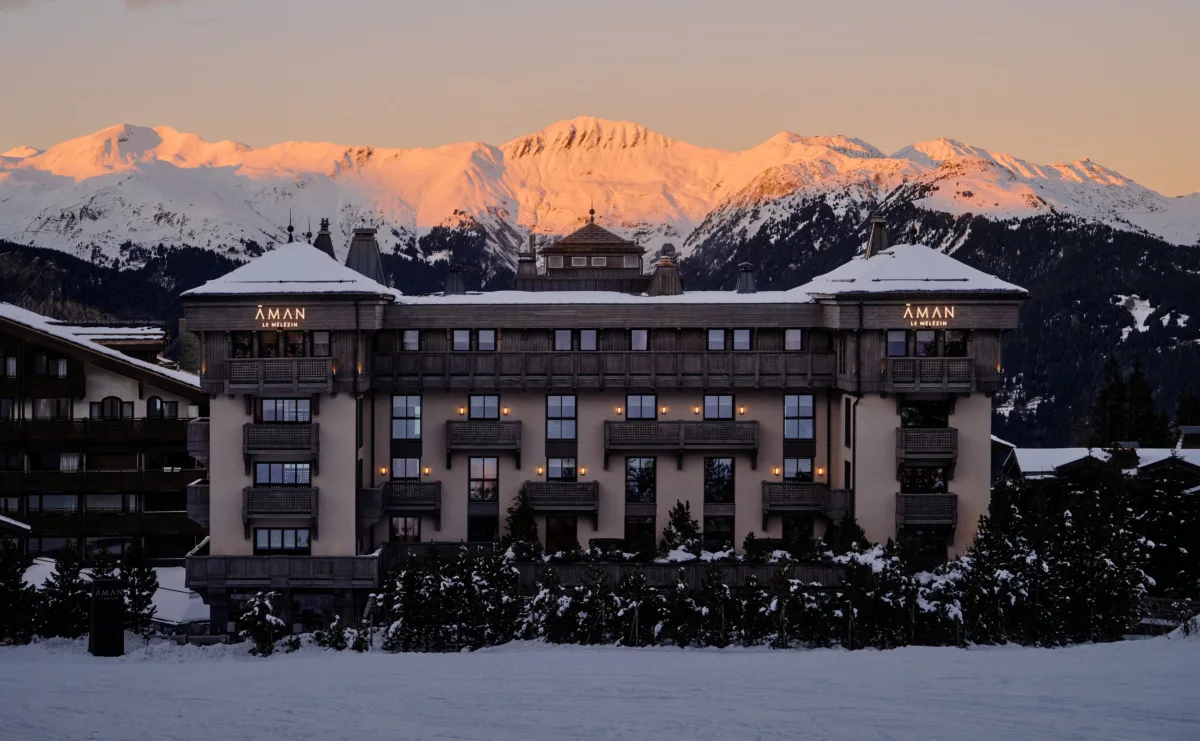 Aman Le Melezin lit at dusk below alpenglow peaks in Courchevel