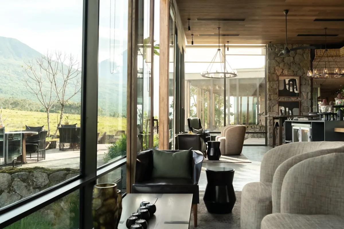 The lounge at Singita Kwitonda Lodge with floor-to-ceiling glass framing the volcanoes of Volcanoes National Park
