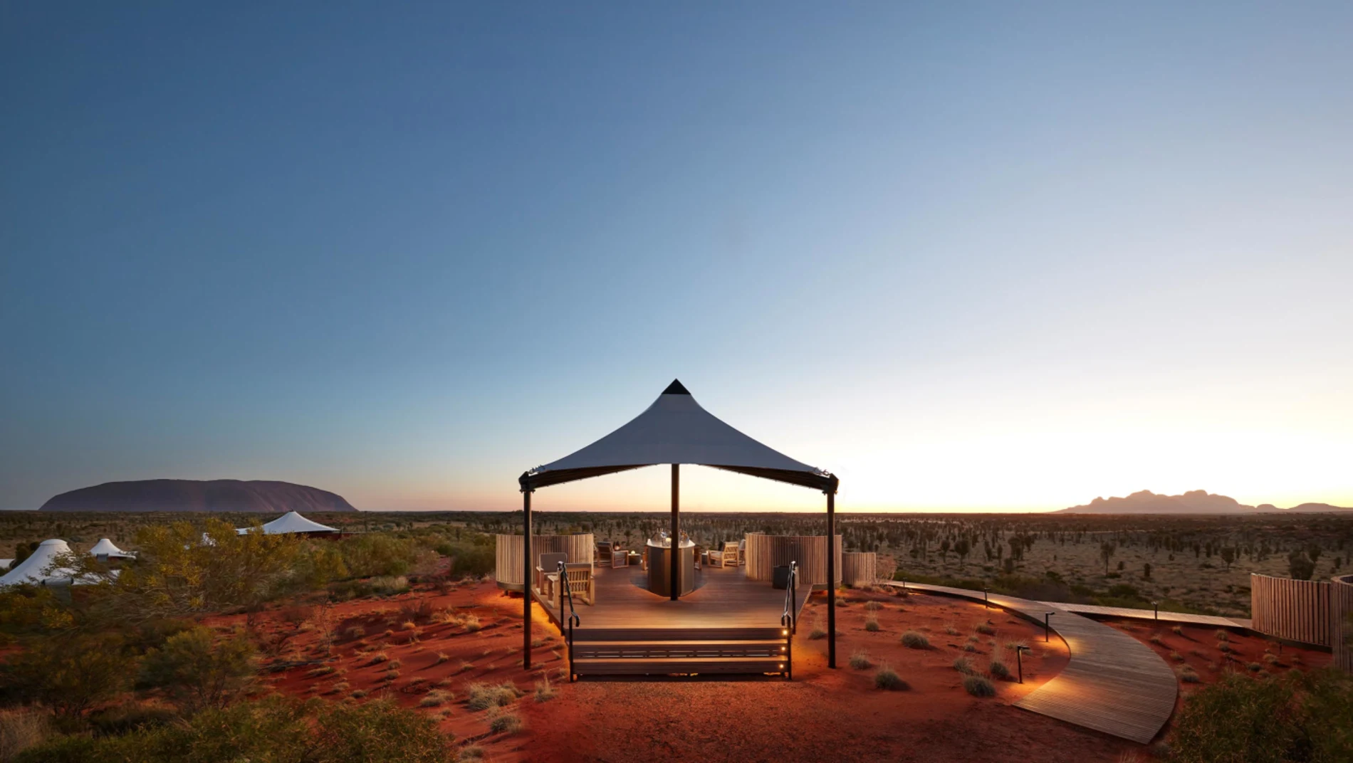 The Dune Top pavilion at Longitude 131 at dusk, with Uluru on the left of the horizon and the domes of Kata Tjuta on the right