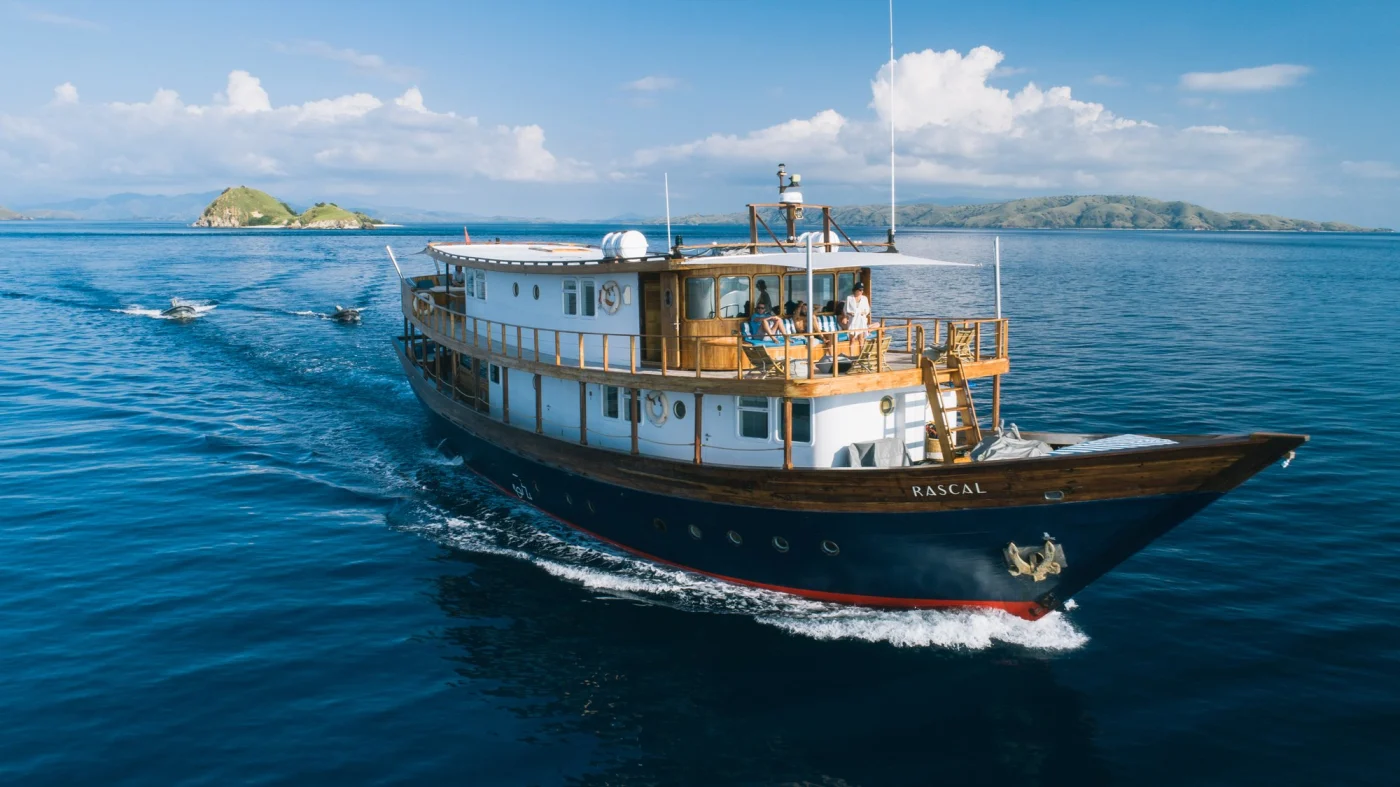 Rascal phinisi yacht sailing through Komodo National Park with guests on the sun deck