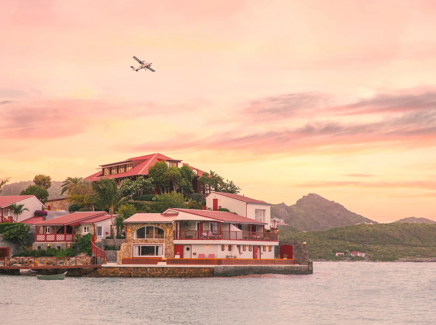 Eden Rock St Barths on its rock in St. Jean Bay at sunset with a small plane landing, the best hotel in St. Barths