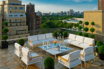 The Mark Penthouse rooftop terrace in New York, with white outdoor sofas, clipped topiary and champagne on a marble table, looking across Central Park to the twin towers of the San Remo