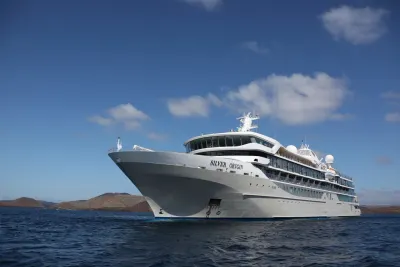 The expedition ship Silver Origin at anchor off a volcanic island in the Galapagos under a blue sky
