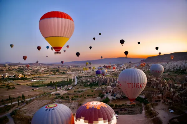 Dozens of colorful hot air balloons rising at dawn over Cappadocia fairy chimney landscape Turkey