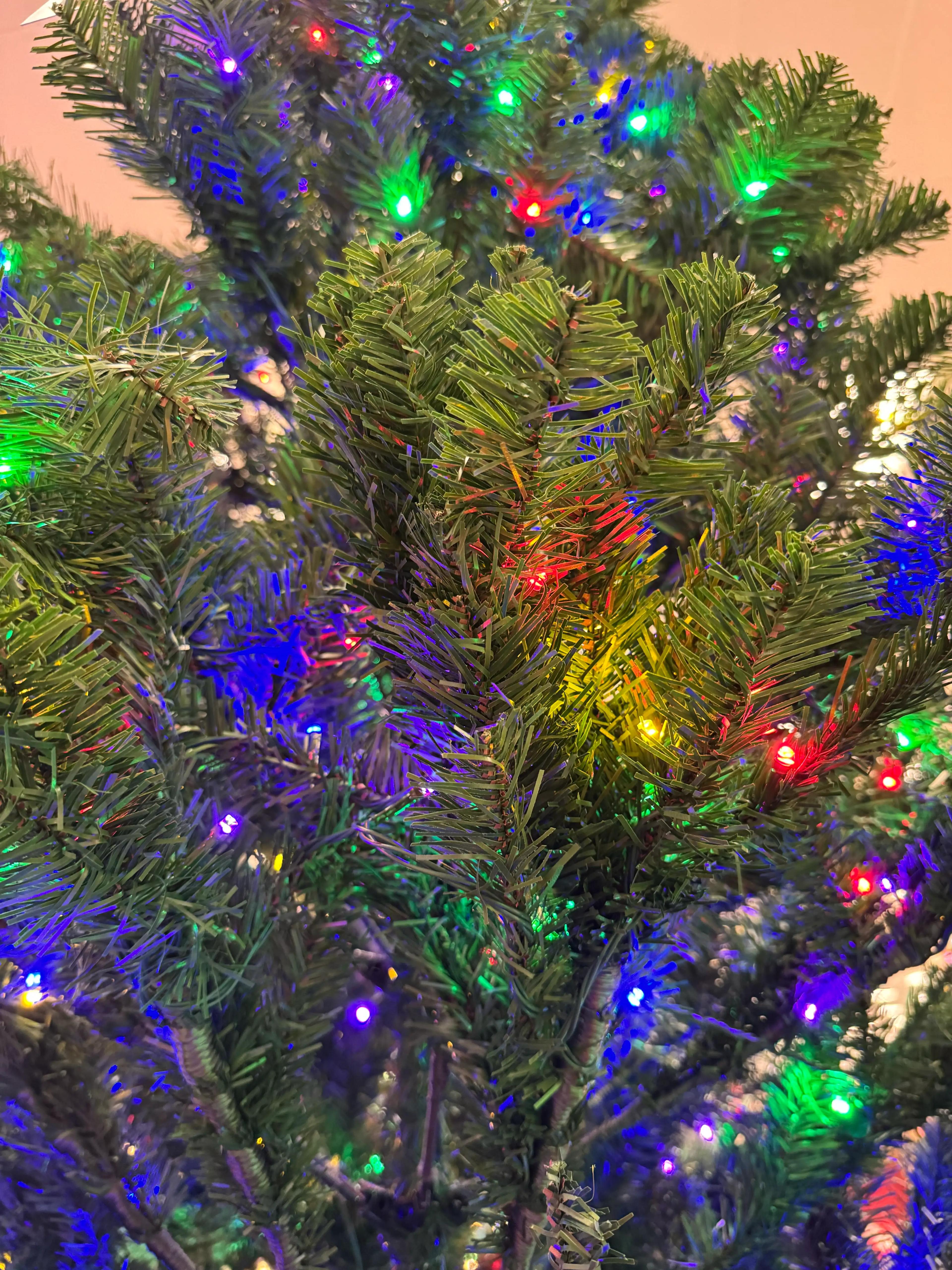 Close-up of sparse PVC spruce branches with multicolor mini lights; visible gaps, thin needle coverage, concentrated light placement on branch tips