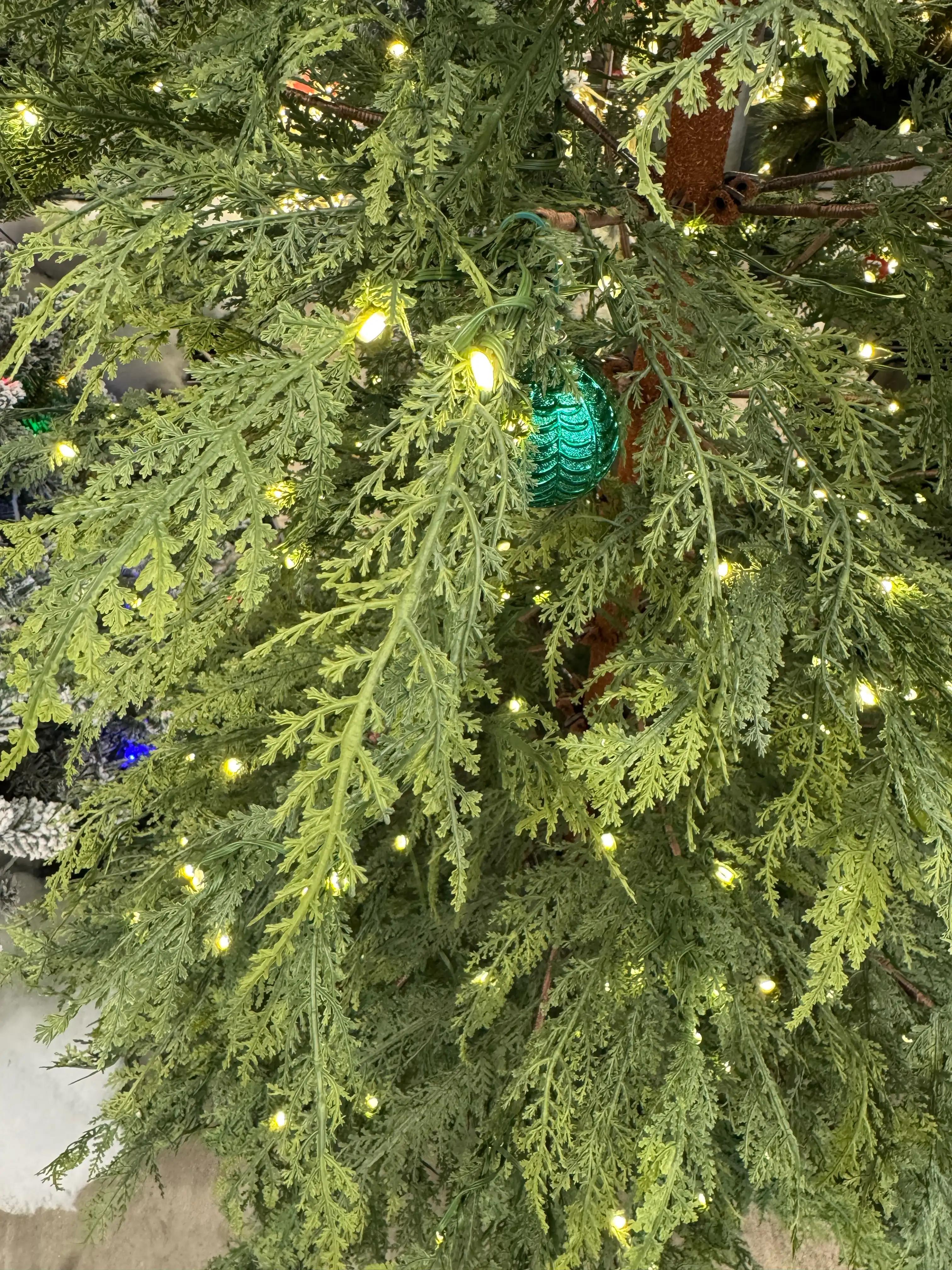 Close-up of realistic molded cypress-style PE branches with sparse warm white mini bulbs, teal ornament visible