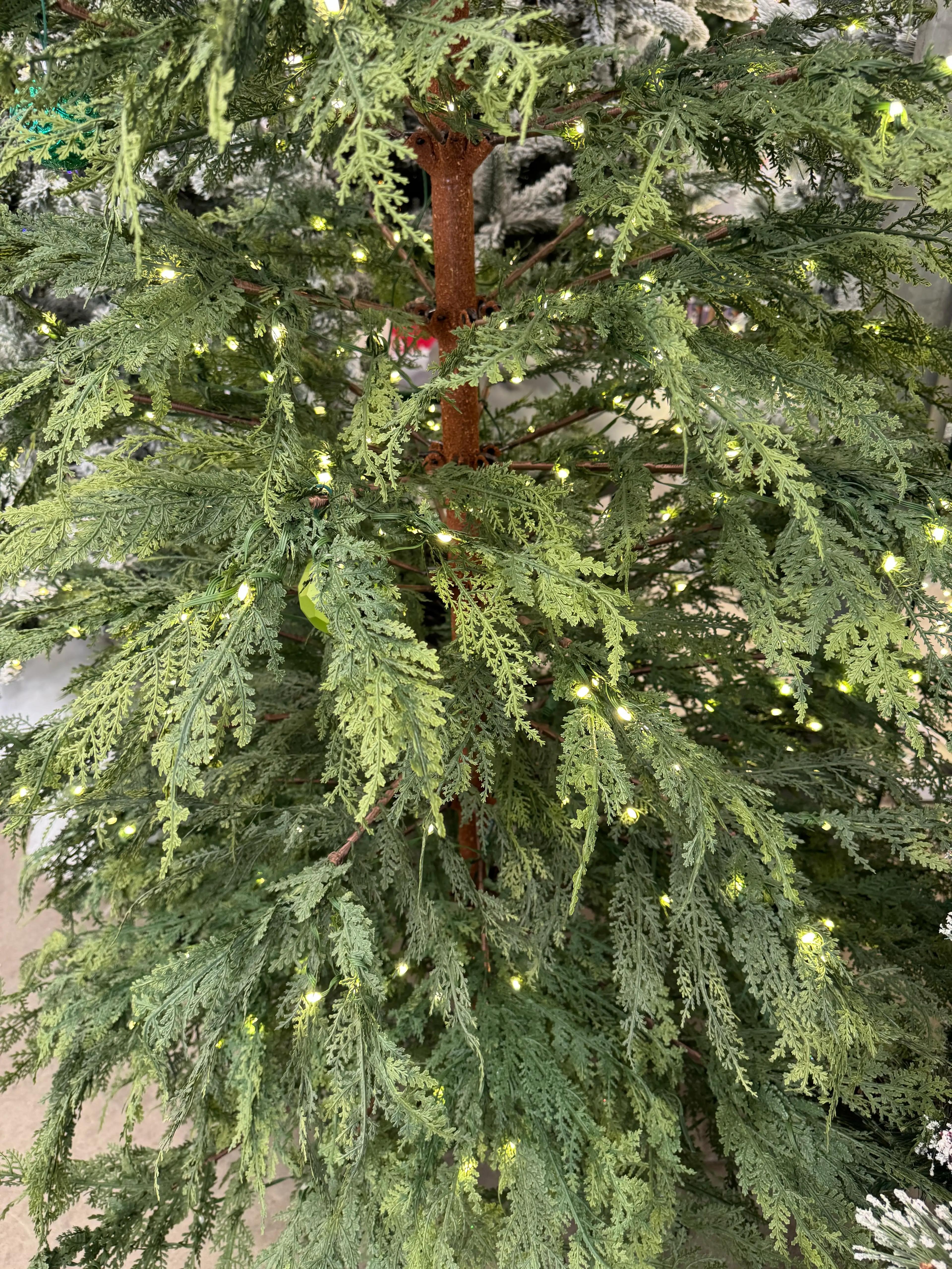 Close-up of dense molded PE cypress-style foliage with warm white micro LEDs, realistic texture, brown trunk visible