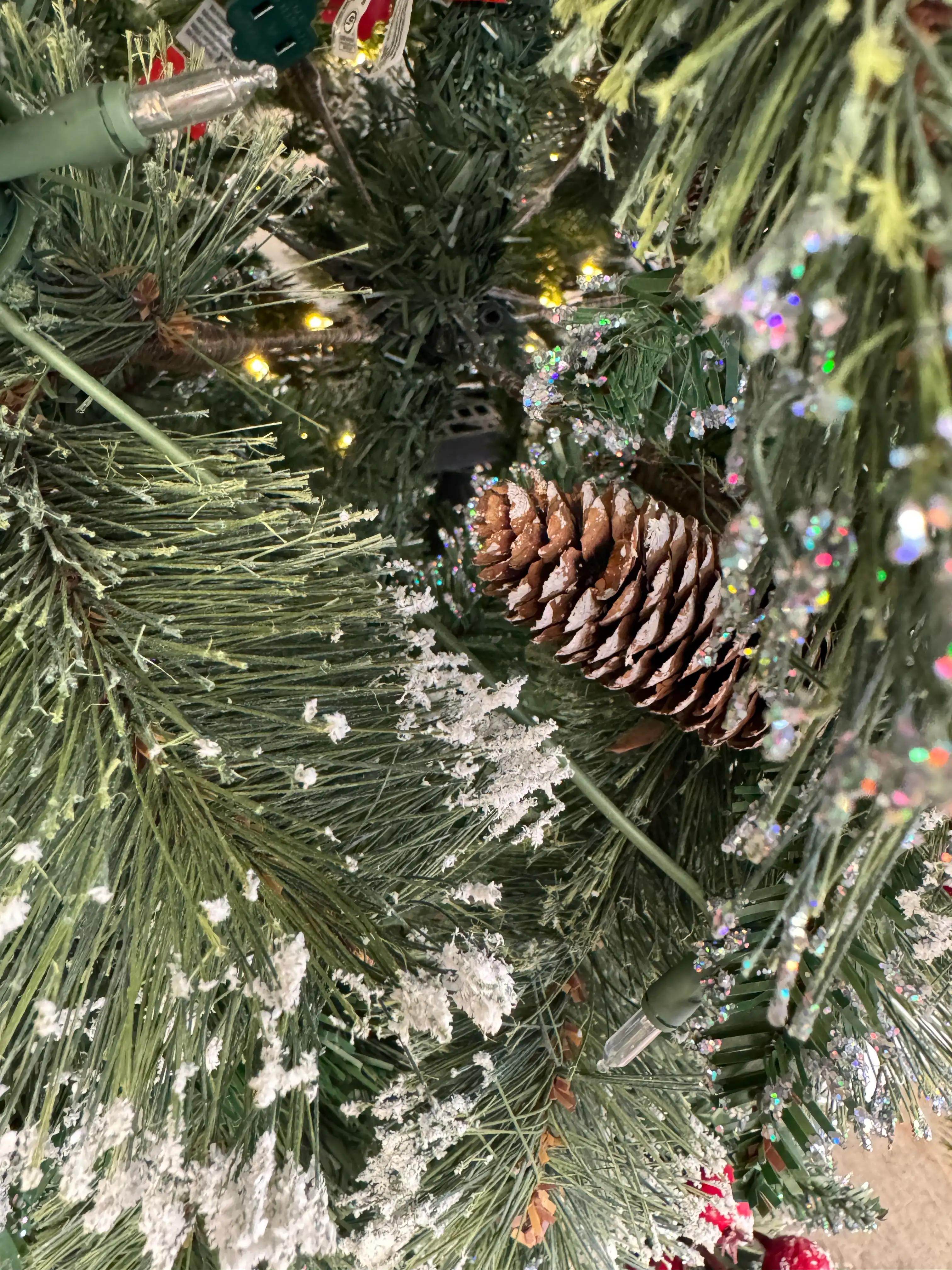 Close-up of frosted PVC pine needles with white glitter coating, brown pinecone, warm LED lights, iridescent tinsel