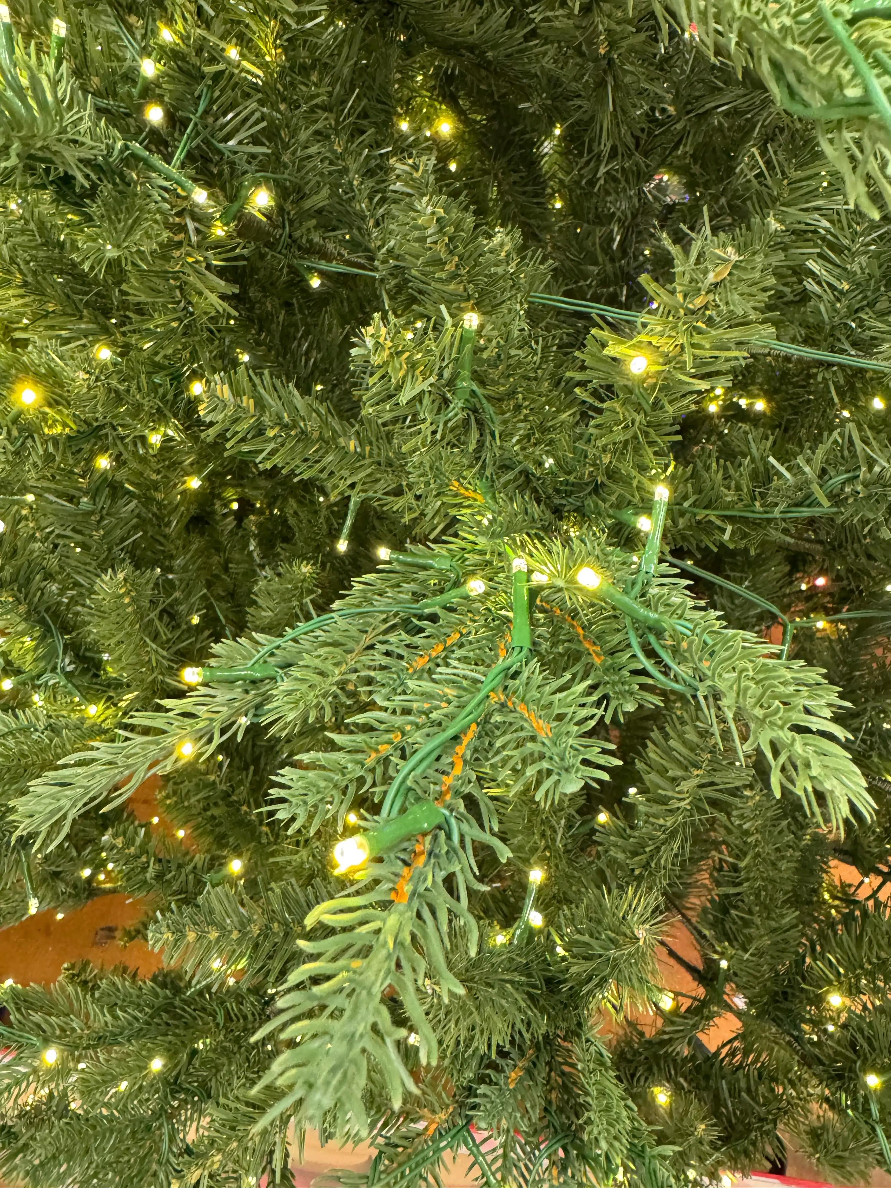 Mixed PVC and molded PE branch tips, warm white LED lights scattered throughout, visible green wire, moderate density