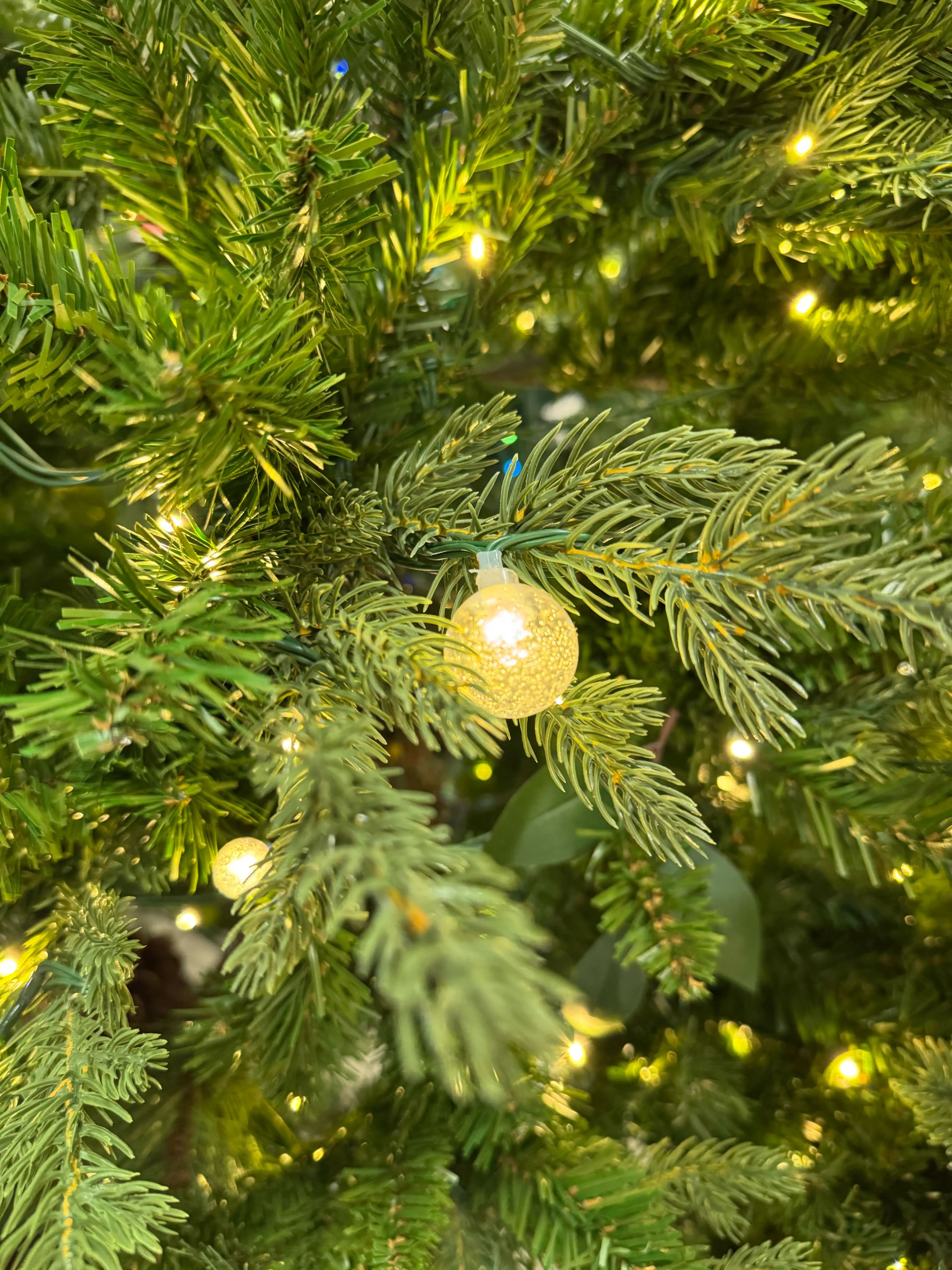 Mixed PVC/PE spruce needles, warm white mini bulbs, textured globe ornament, moderate density with some visible gaps