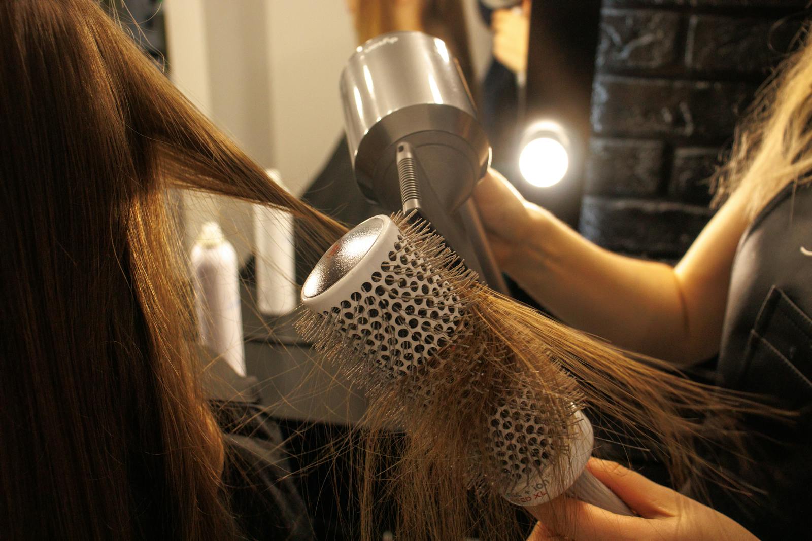 Stylist using a round brush and blow dryer to style a client's hair in the salon