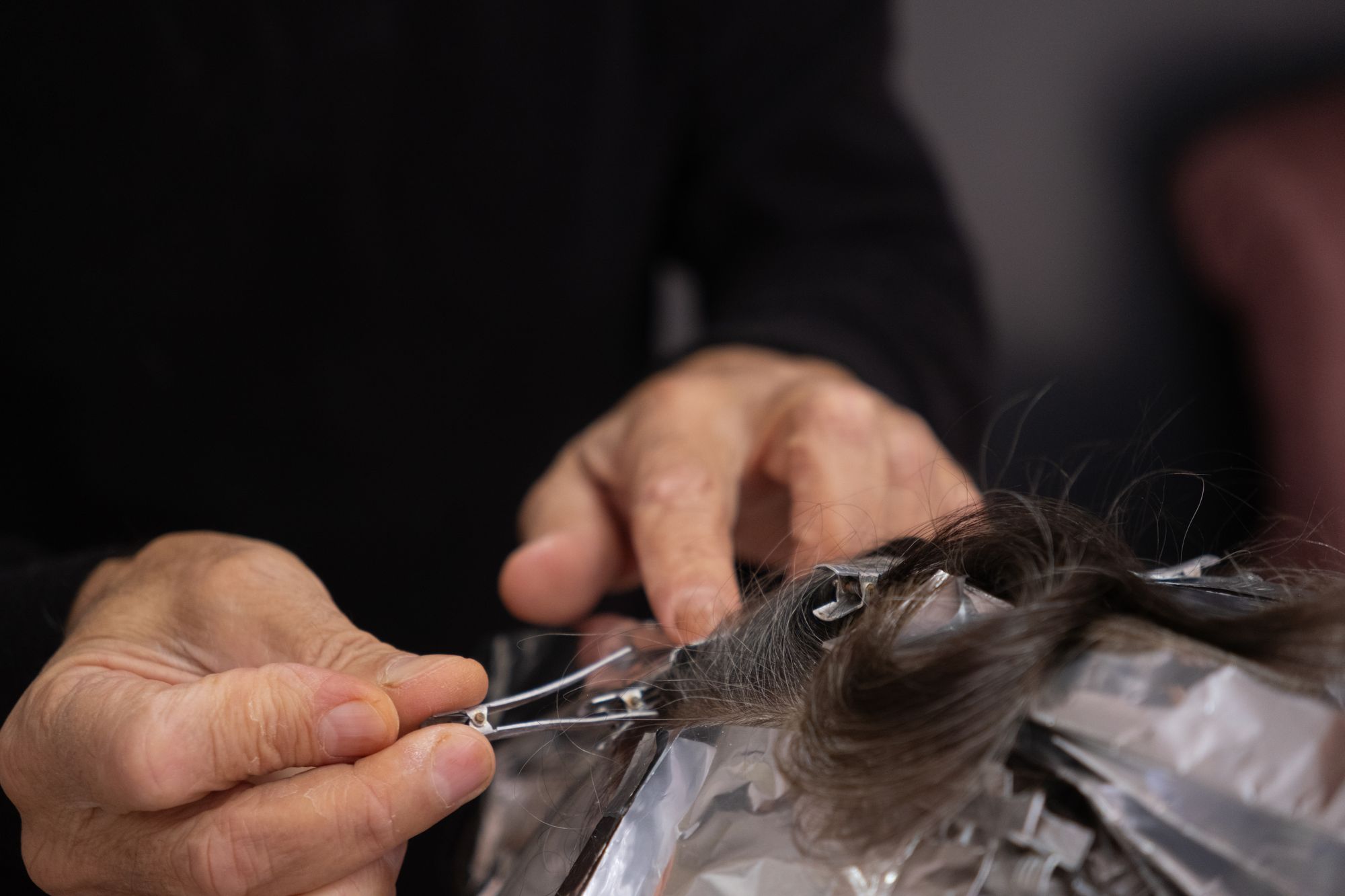 Close-up of foils being clipped into gray-streaked hair during a highlight service