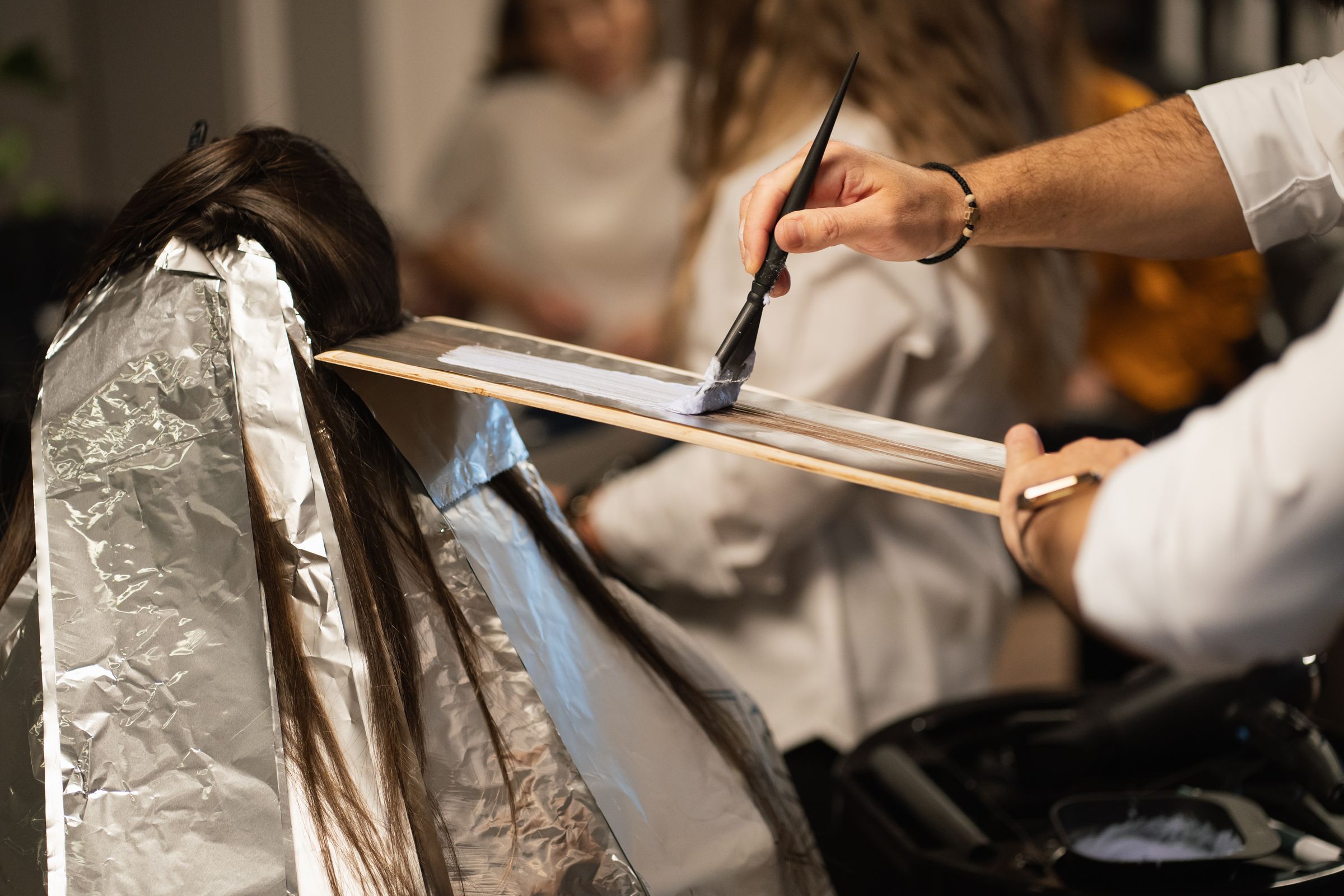 Colorist sweeping lightener freehand down a section of hair laid over a balayage board