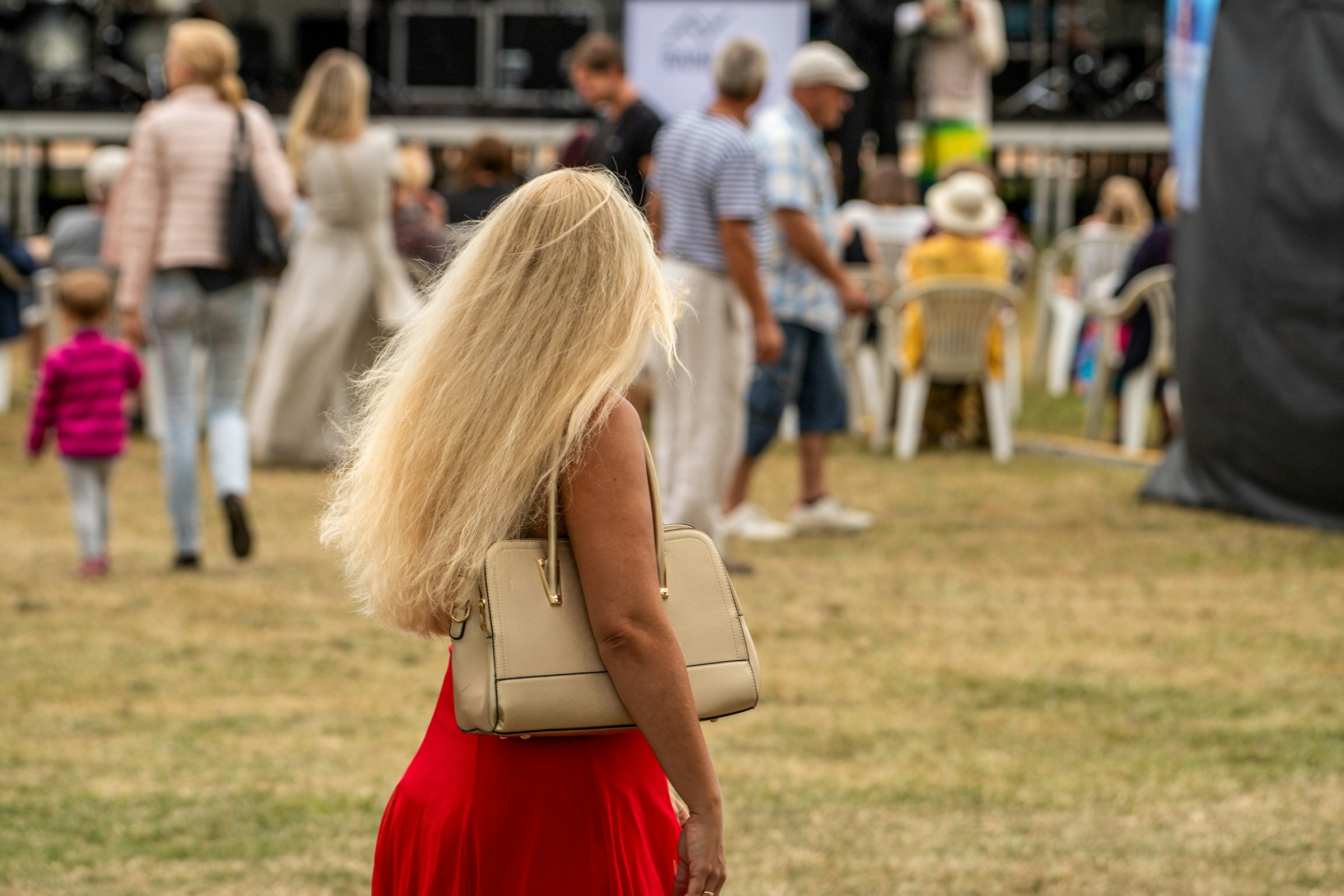 Woman with long blonde hair walking across the grass at an outdoor music festival