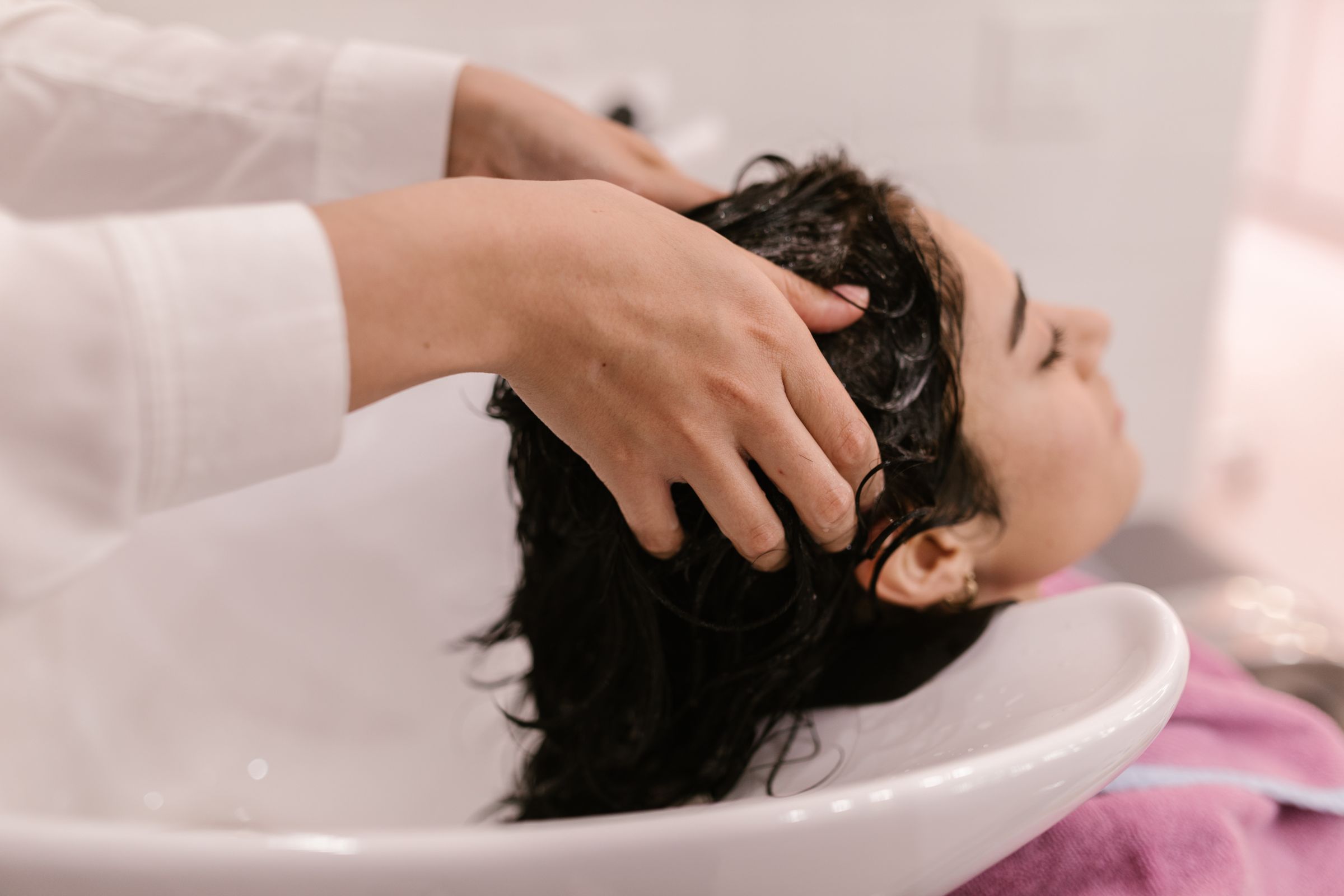 Stylist massaging a guest's scalp at a white salon shampoo bowl