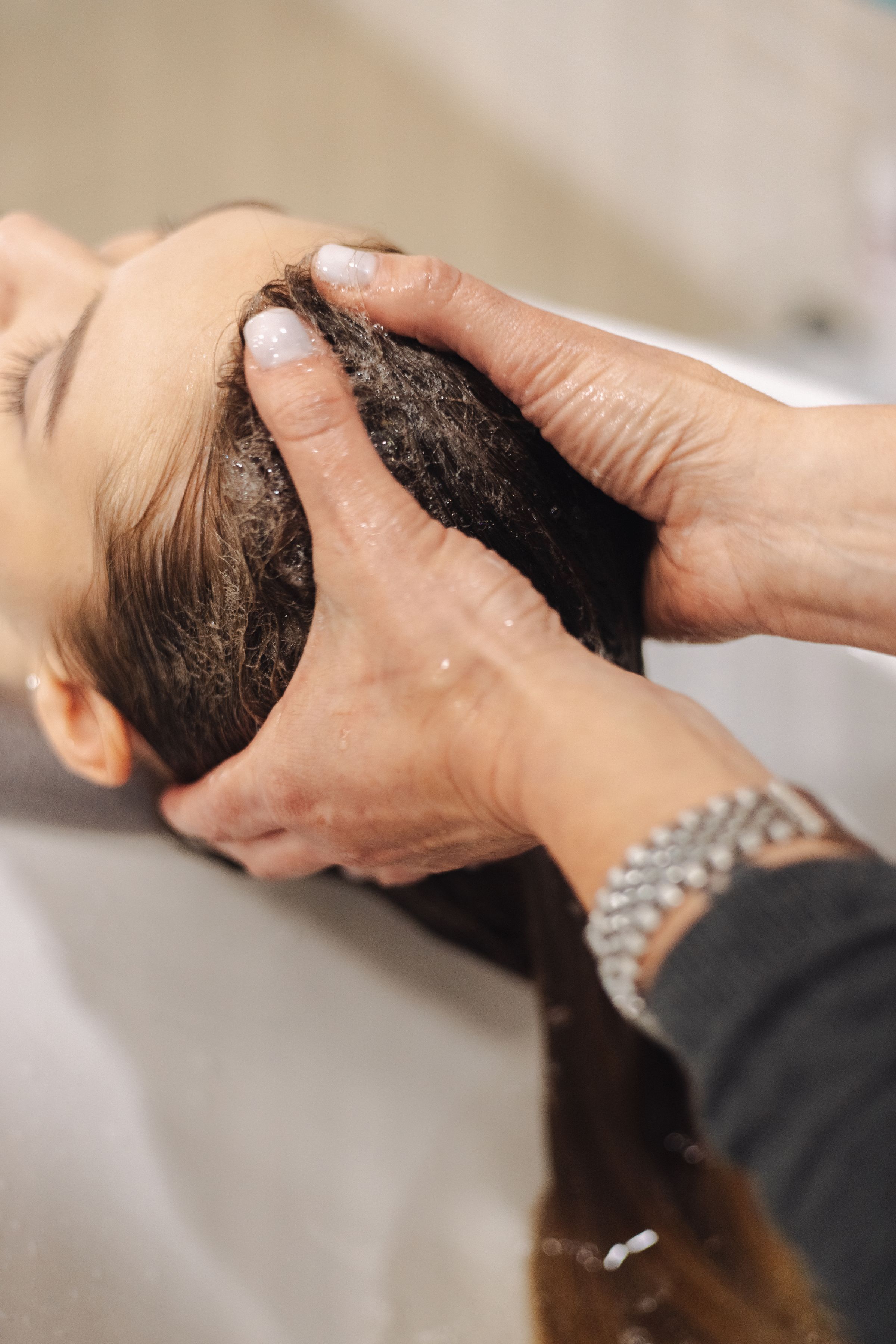 Stylist's hands massaging shampoo into a guest's scalp at the shampoo bowl