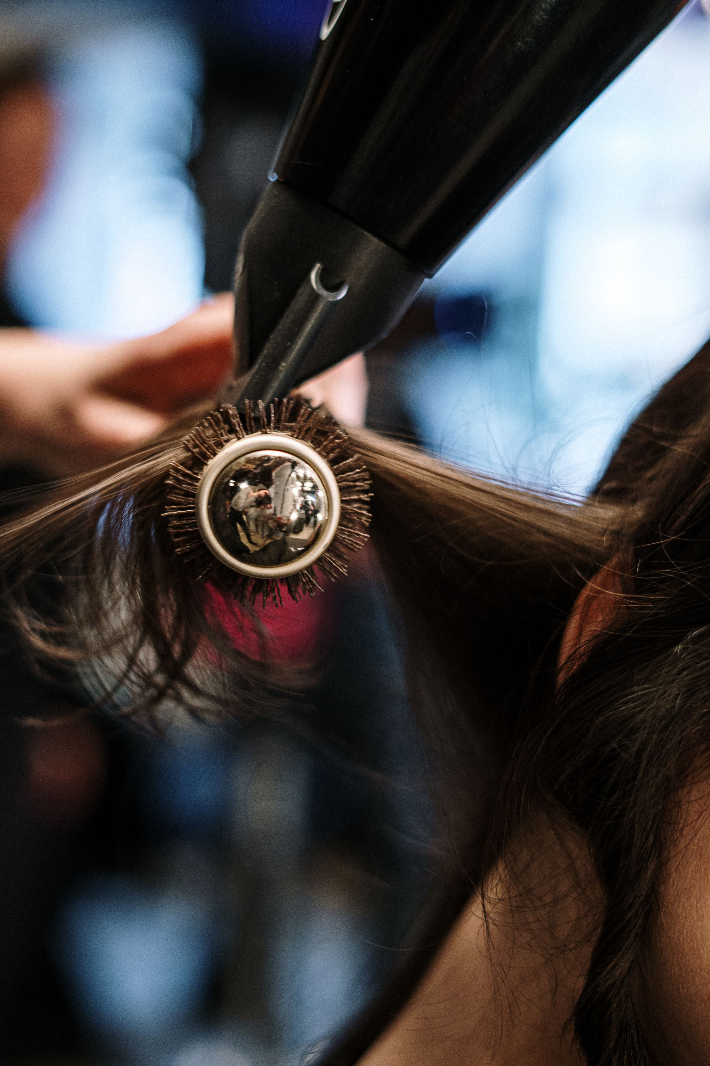 Close up of a round brush and blow dryer smoothing a section of dark hair