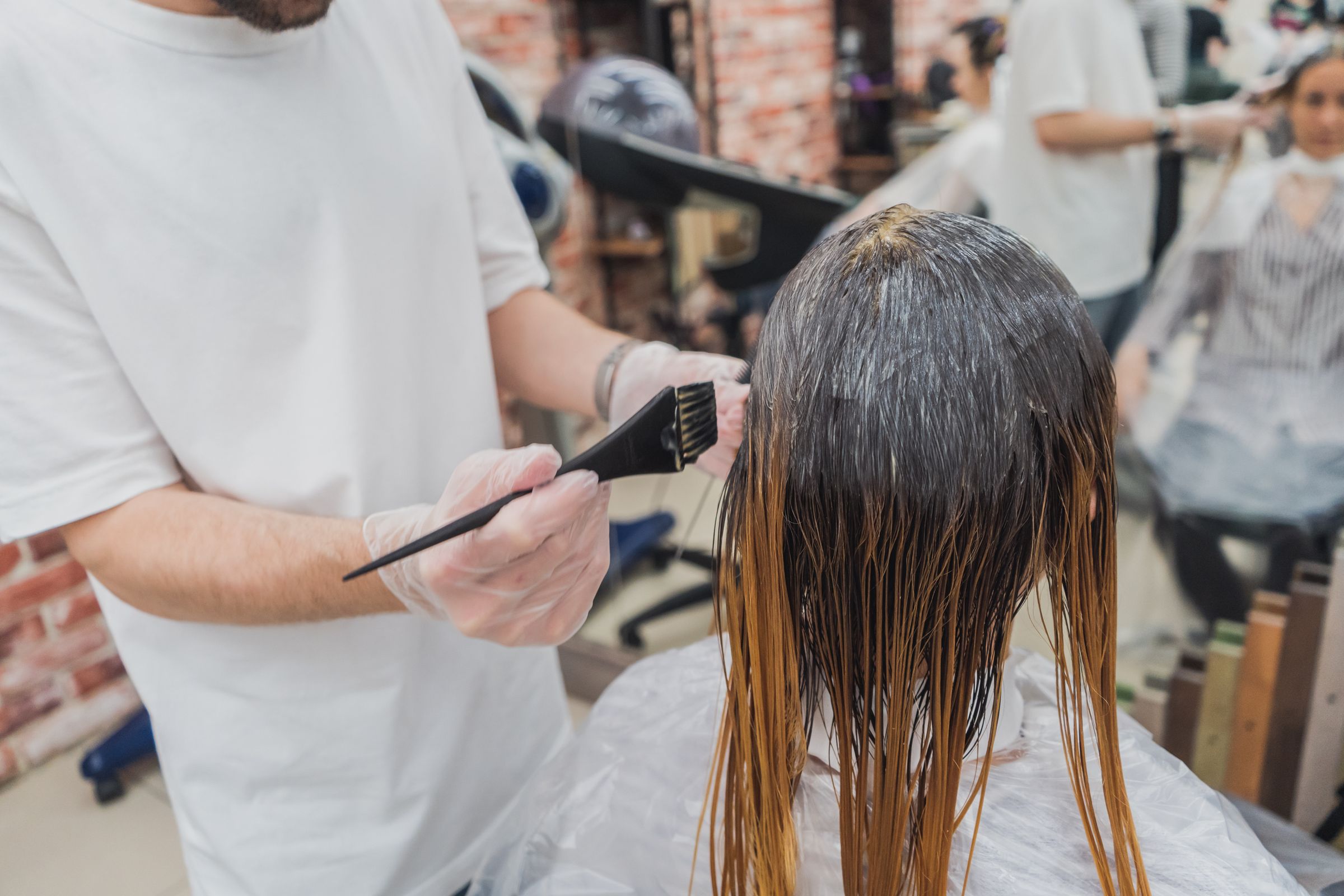 Colorist brushing hair color through a client's long hair at the salon chair