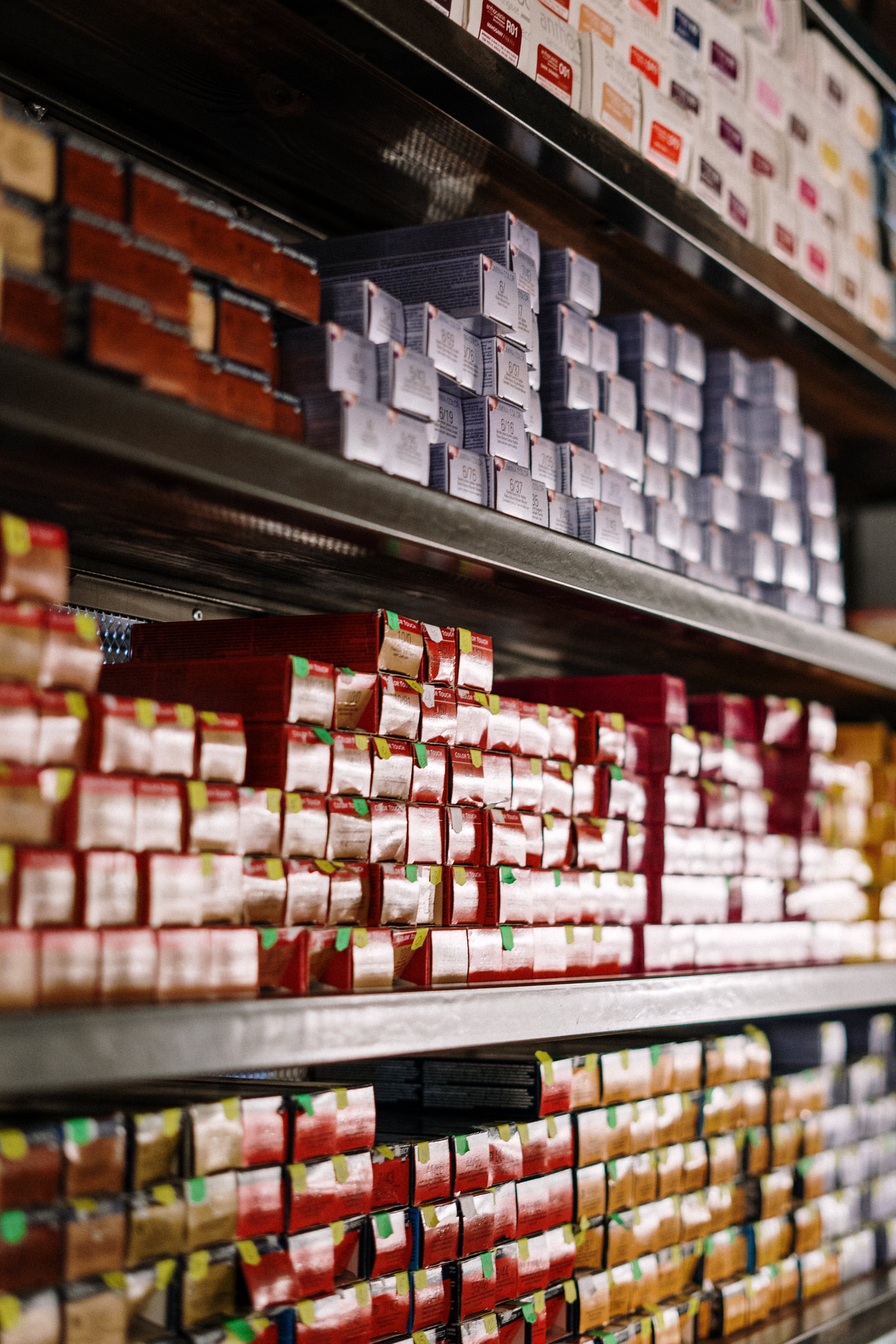 A moody and mystical close-up of hair dye boxes of various shapes, colours, and brands arranged on shelf in a hair salon.