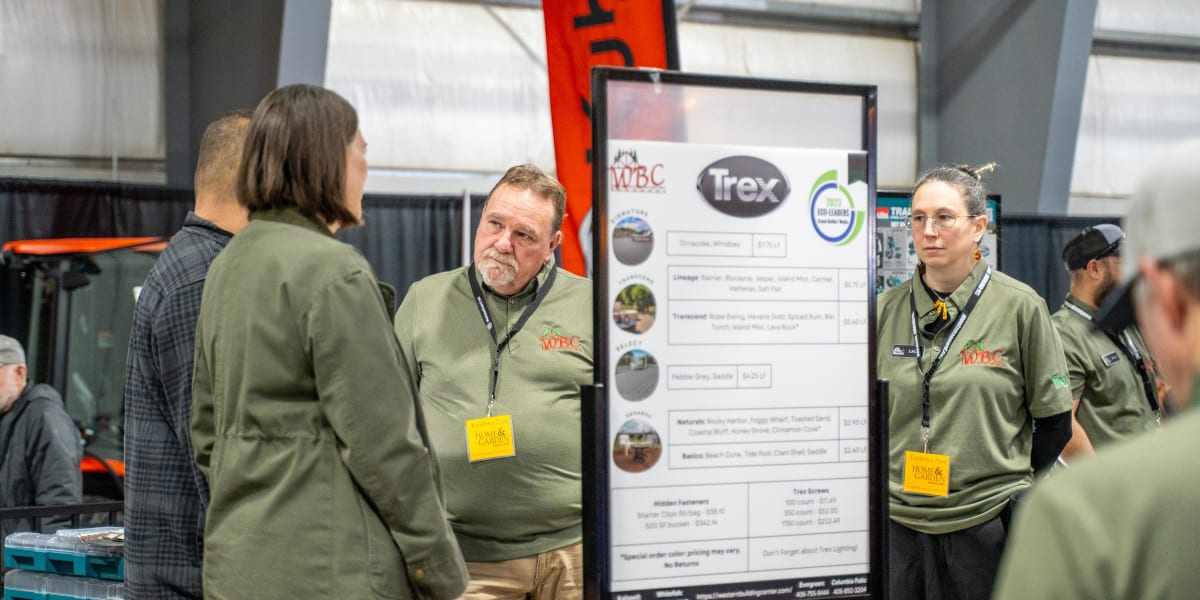 Western Building Center employees in olive green company shirts are presenting at a trade show booth featuring Trex decking p