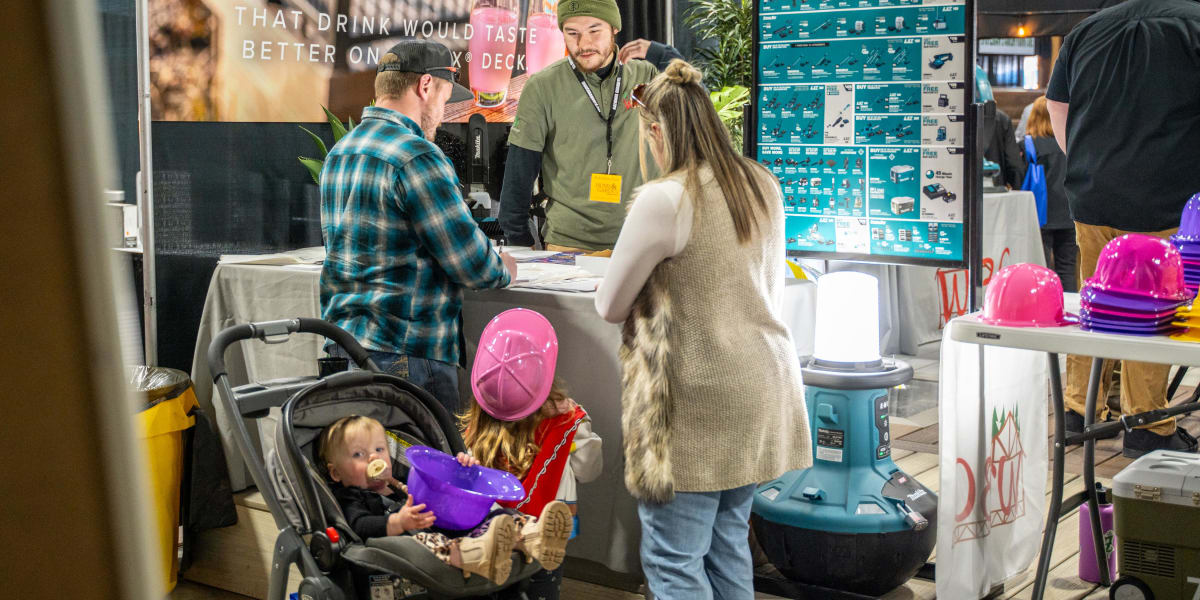 A family with a baby in a stroller visits a trade show booth featuring Trex decking products and Makita tool promotions