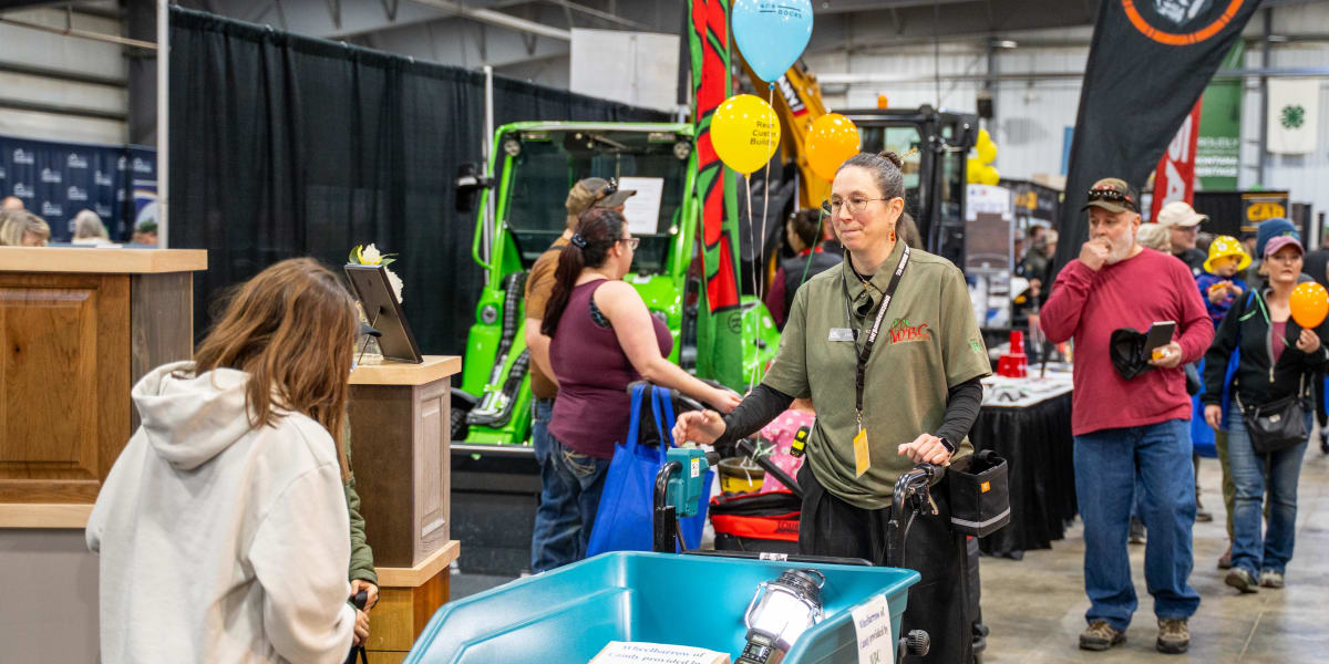 Western Building Center staff member in olive green company shirt with WBC logo interacting with visitors at an indoor trade