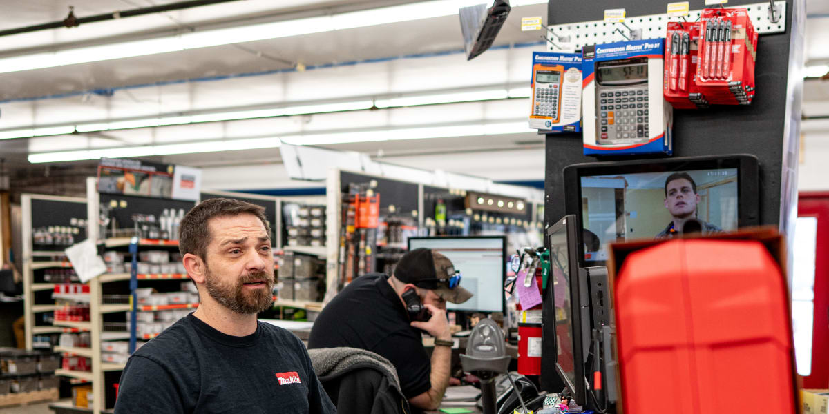 A customer service interaction at the checkout counter where an employee in a dark shirt is helping a customer who is holding