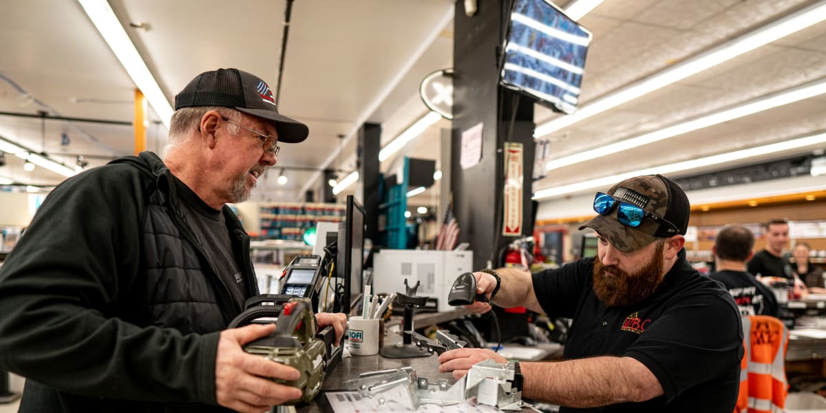 Two men are engaged in a customer service interaction at what appears to be a checkout counter or service desk inside a Weste