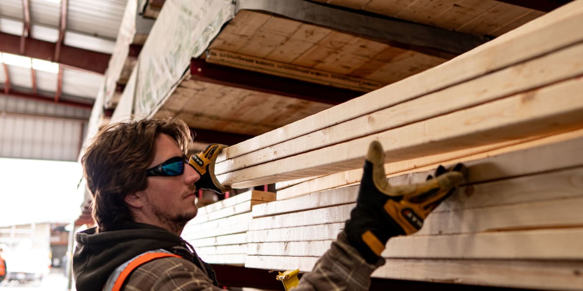 A warehouse worker wearing safety glasses, work gloves, and a high-visibility orange safety vest is selecting or organizing d