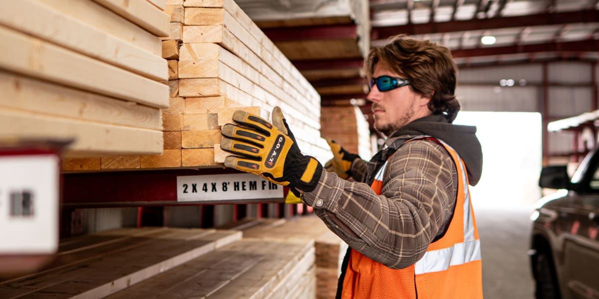 A warehouse worker in safety gear examining and handling dimensional lumber in an indoor lumber storage facility