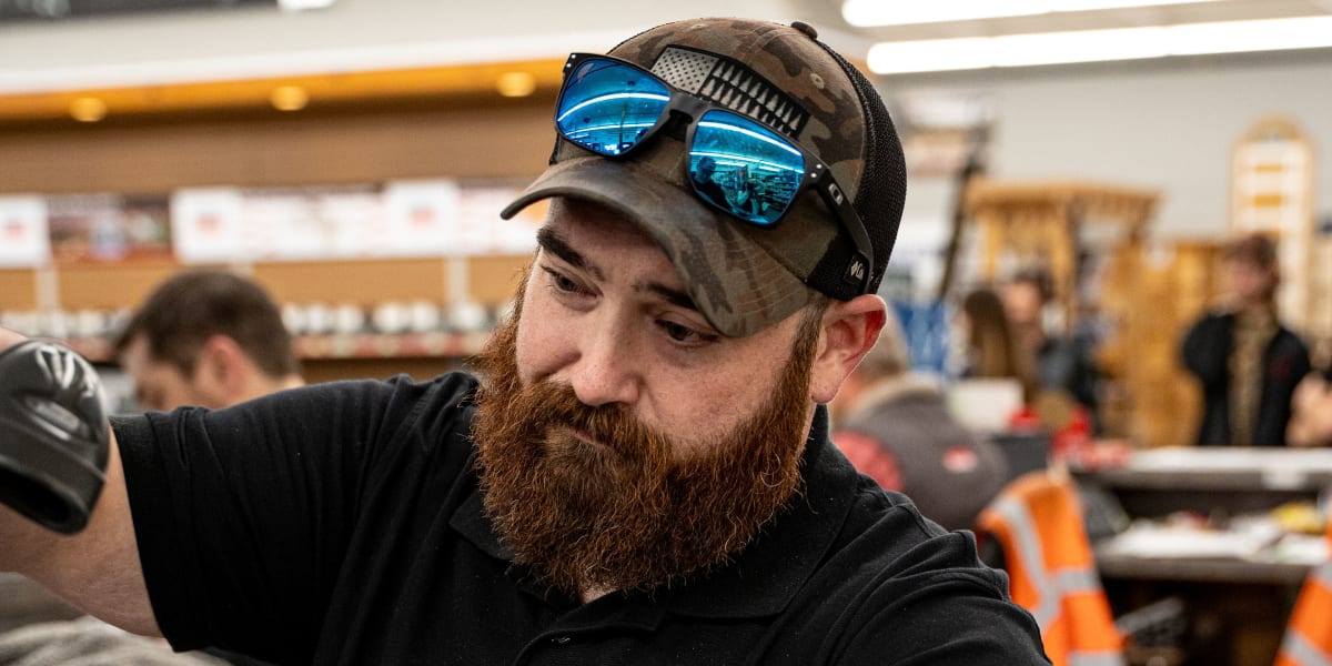 A bearded employee wearing a black WBC polo shirt and camouflage cap with blue mirrored sunglasses is working at what appears