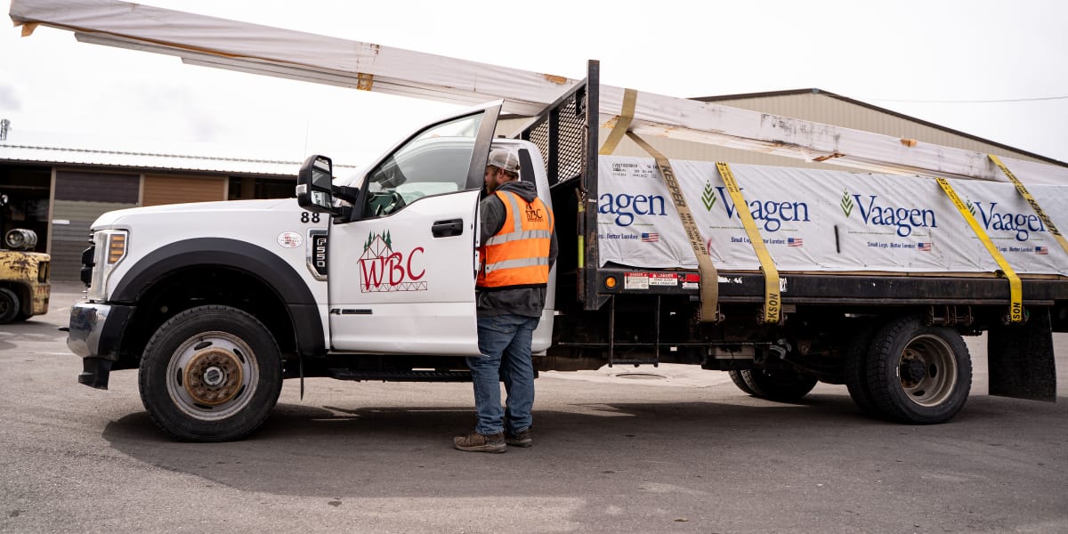 A WJBC delivery driver in an orange safety vest stands next to a white Ford truck loaded with building materials including lu