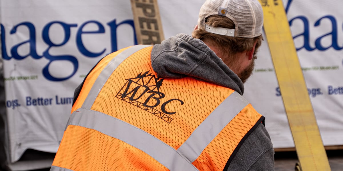 A construction worker wearing an orange high-visibility safety vest with reflective stripes and a baseball cap is working at