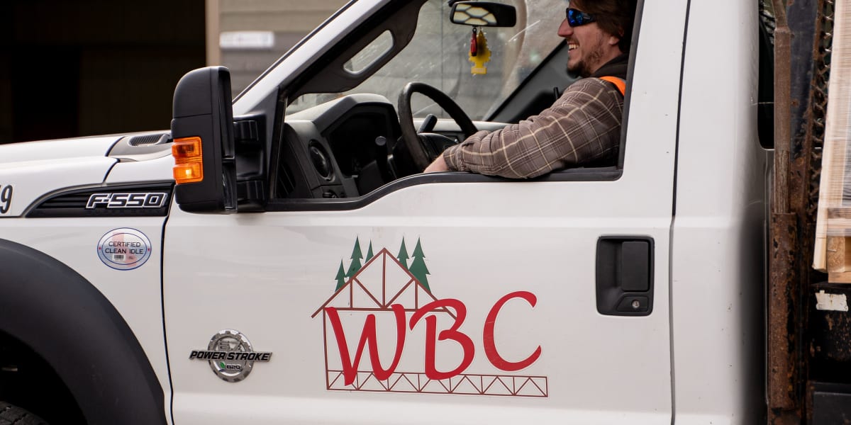 A smiling WBC employee sits in the driver's seat of a white Ford F-550 work truck with the Western Building Center logo promi