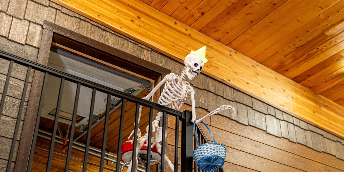 A Halloween-themed display featuring a skeleton decoration positioned on a wooden balcony or loft area inside what appears to